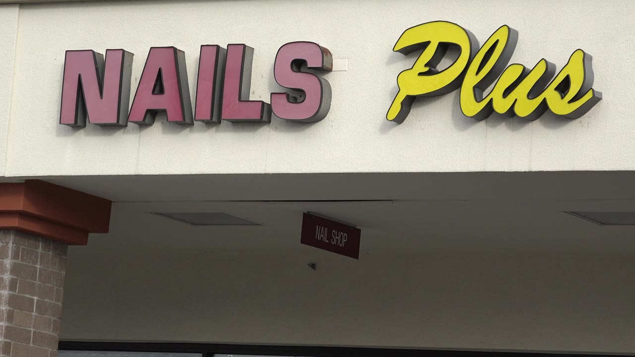 Close composition on the Nails Plus lettering in Westminster, Colorado, with the sign filling the upper storefront and the shaded walkway below, no visible people.