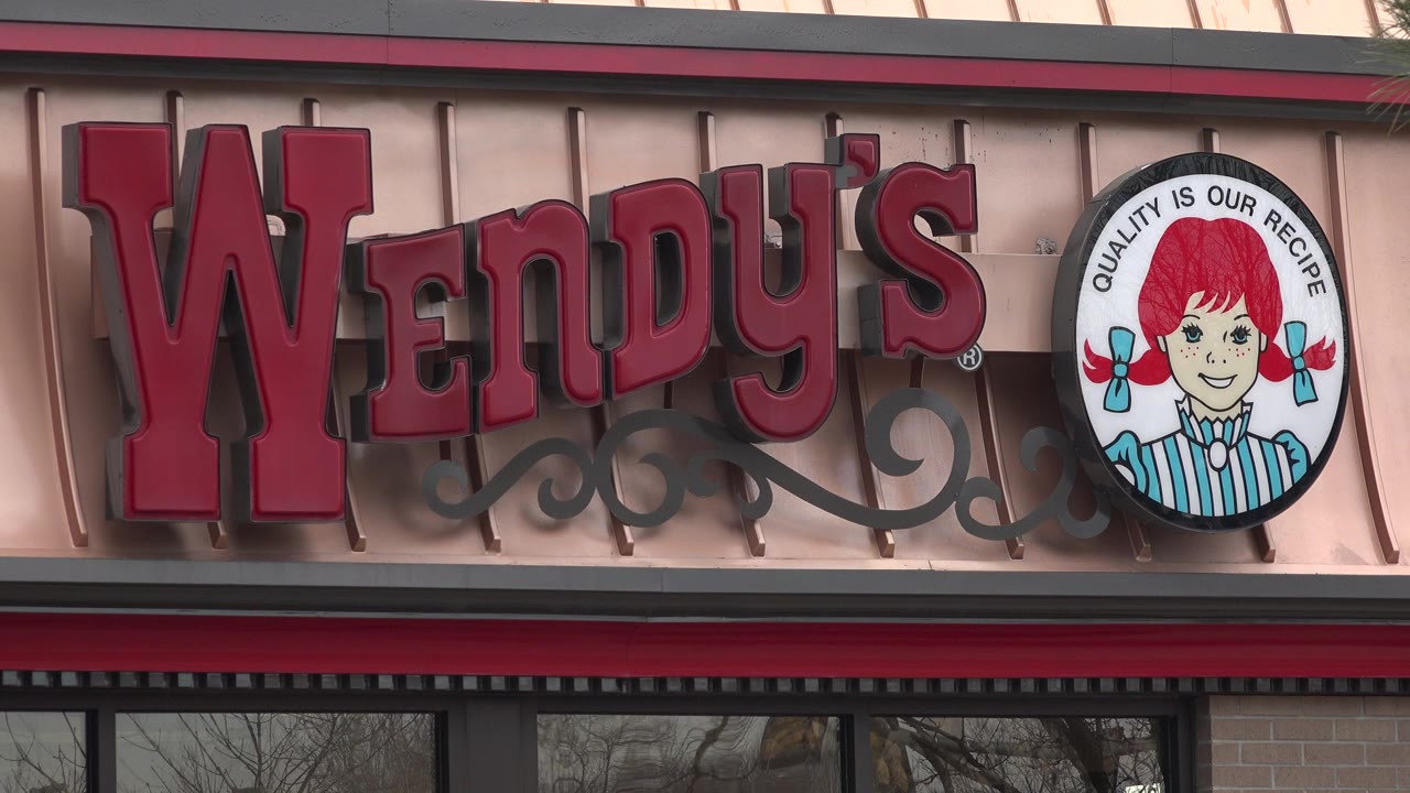 Close view of a Wendy's sign and round logo on a restaurant facade in Westminster, Colorado, with dark window reflections below and no visible people.