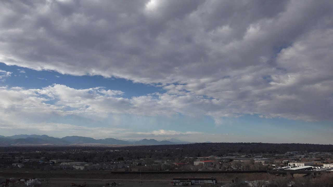 Opening frame in Westminster, Colorado showing heavy gray-white clouds above a narrow suburban horizon and distant mountains, with no visible people.
