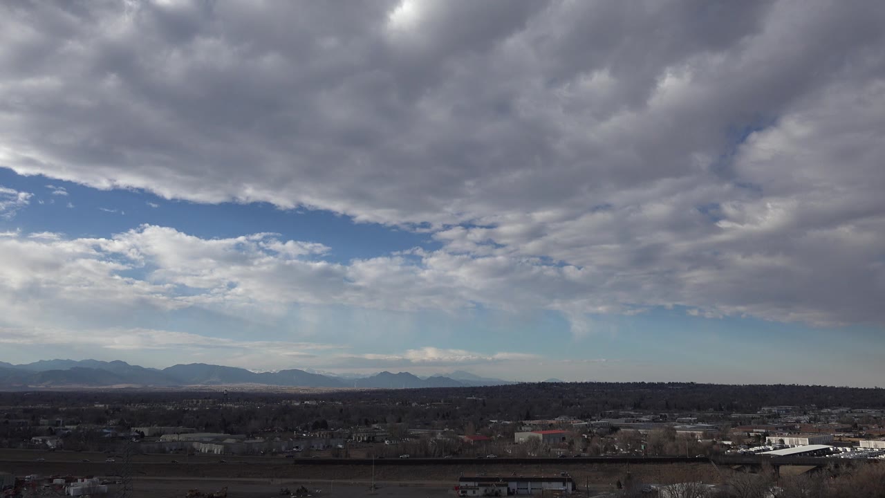 Layered stormlike clouds above distant mountains and suburban buildings