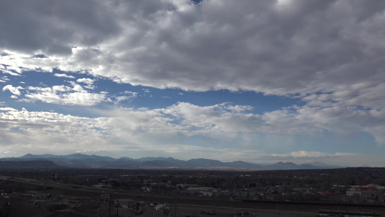 Opening frame of Westminster, Colorado with a dark suburban foreground, distant mountains, heavy gray clouds, blue sky gaps, and no visible people.