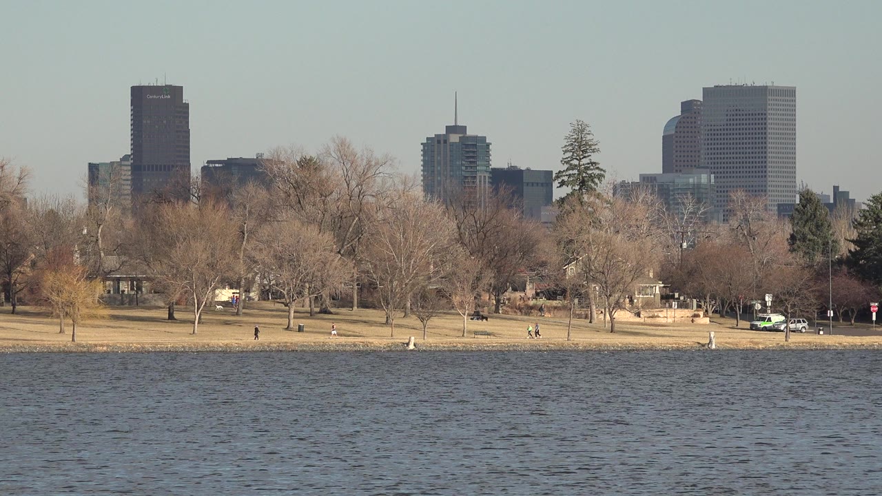 Lake water, park shoreline, bare trees, distant walkers, and city buildings.