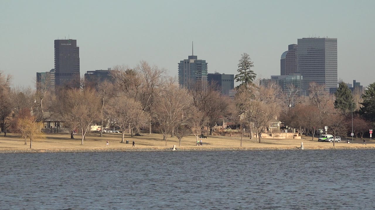 Lake water, park trees, small walkers, and distant city buildings.