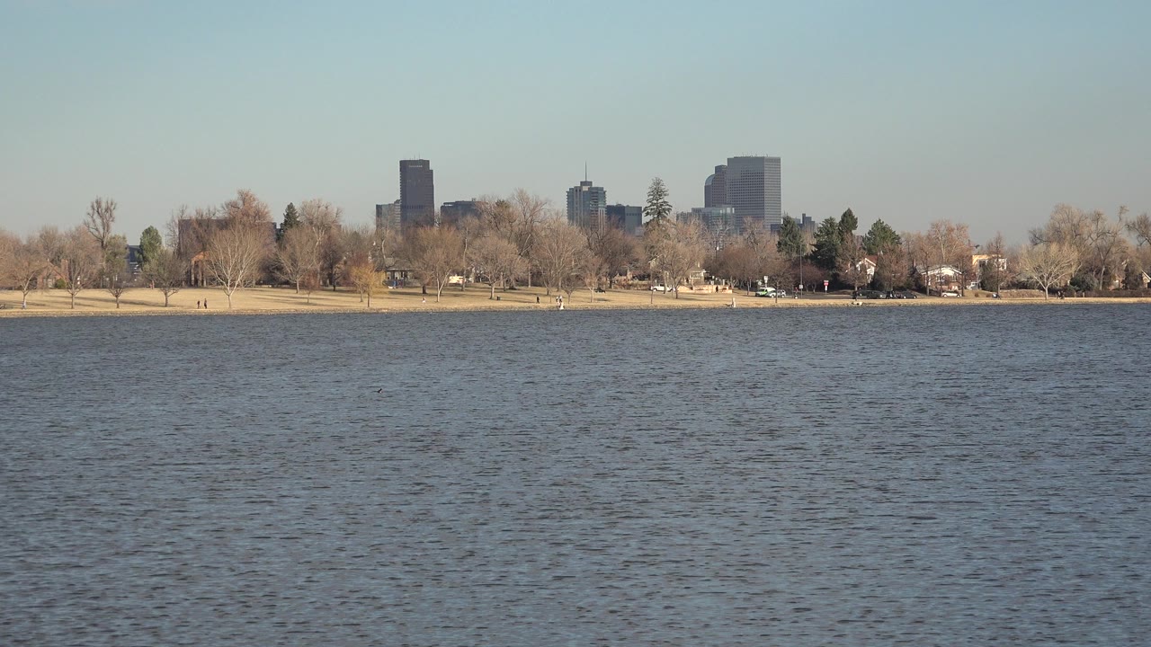 Wide lake view with distant shoreline, bare trees, and city buildings.
