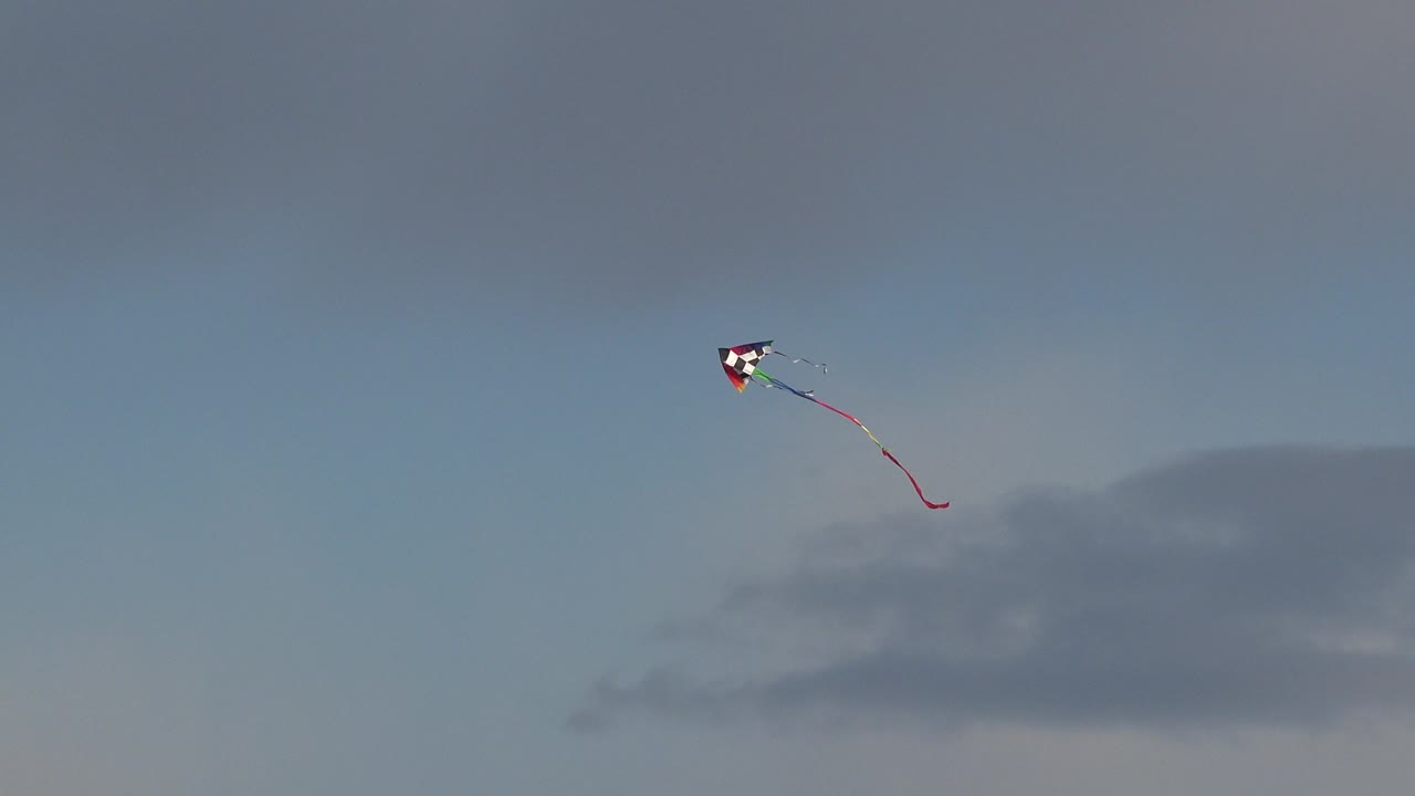 At 0:01 in Westminster, Colorado, the kite appears near the upper frame with its red tail curving downward over muted clouds, and no visible people are present.