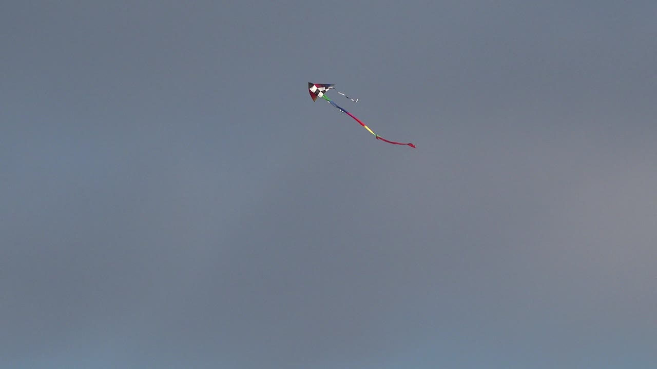 A small multicolored kite appears near the upper left of a gray-blue sky in Westminster, Colorado, with no visible people.