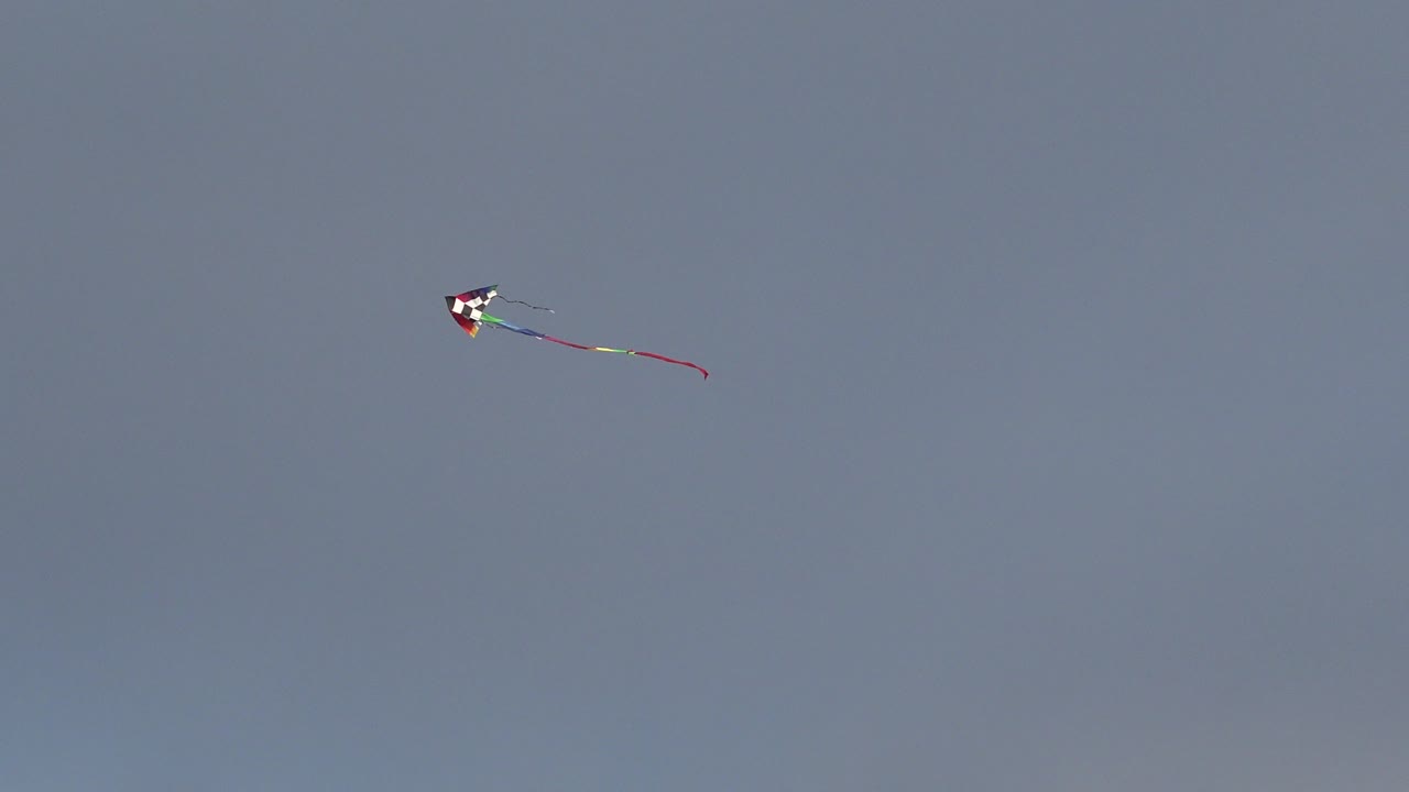 At 0:00, a small multicolored kite with a trailing red tail sits high in the Westminster, Colorado sky with no visible people.