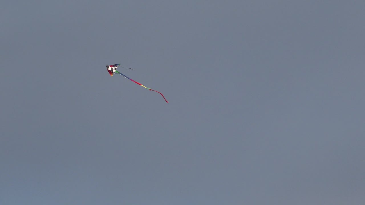 Small kite near the top of a cloudless sky with a curved red tail.