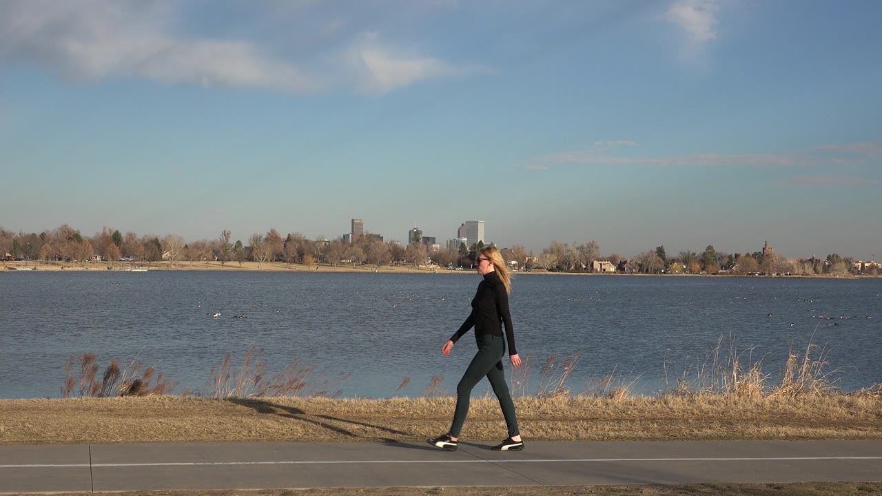 Woman walking on a paved path beside open water.