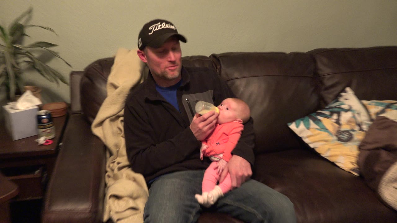 Two seconds in, the composition shifts slightly right in the contact sheet, showing the baby tilted back in the father's arm while the bottle remains at the infant's mouth.