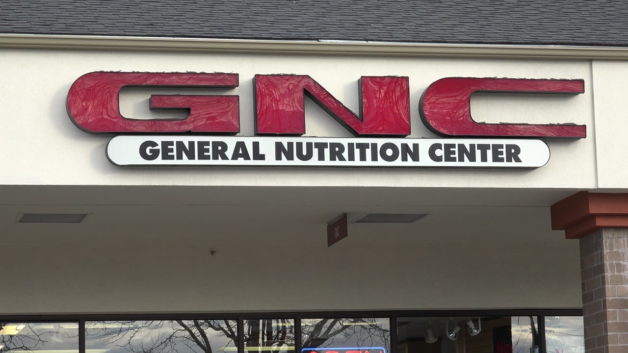 The Westminster storefront remains centered on the red GNC sign, with the General Nutrition Center panel, shaded walkway, glass windows, and brick column visible below.