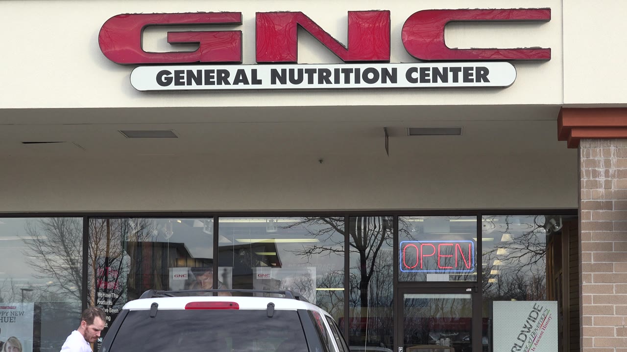 GNC storefront with white SUV parked outside and a man nearby