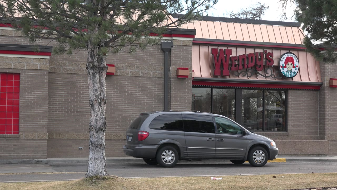 Wendy's restaurant exterior with a gray minivan in front and trees along the road.