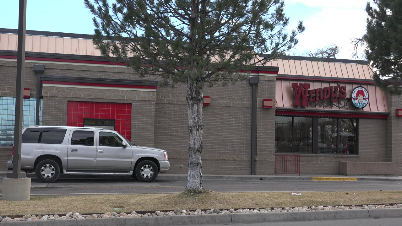 The Westminster restaurant facade remains centered with the Wendy's sign visible, a silver SUV in the lot, a pine tree trunk near center, and no clearly visible pedestrians.