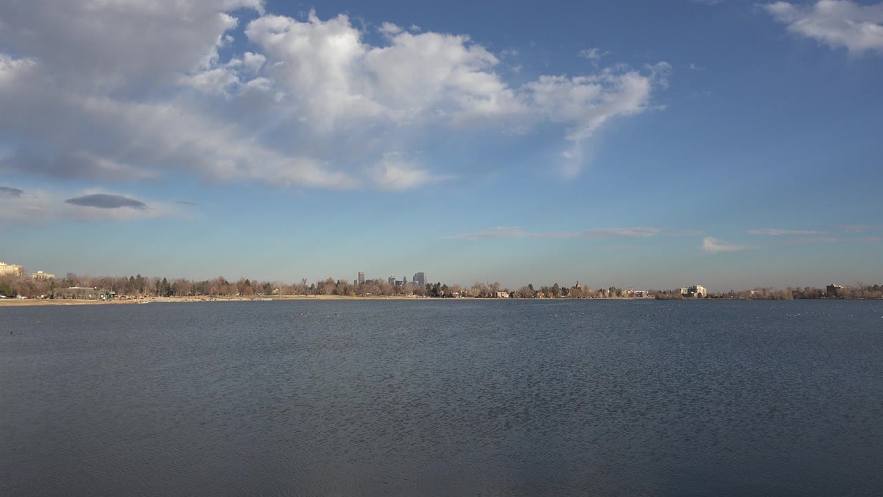 Westminster, Colorado waterfront frame with textured water in front, a thin tree-lined shore, small distant buildings, and no visible people.