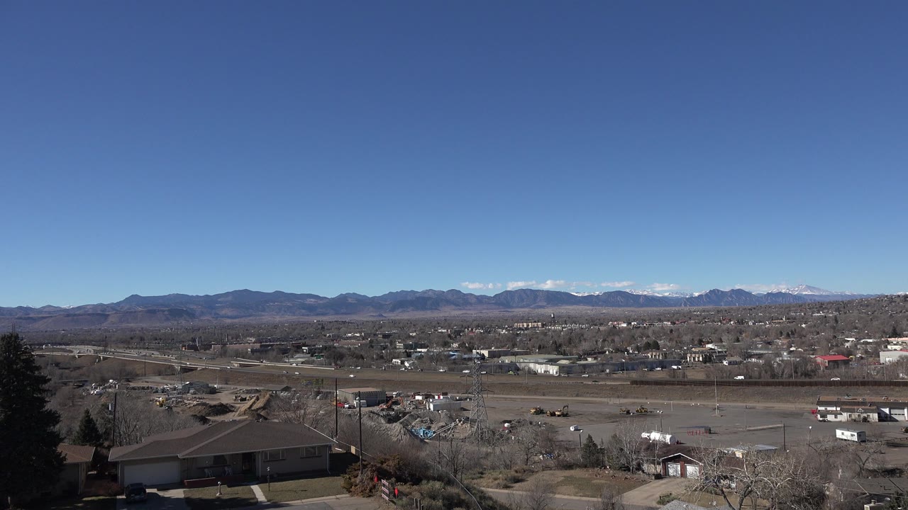 Elevated suburban view with roads, low buildings, leafless trees, and distant mountains.