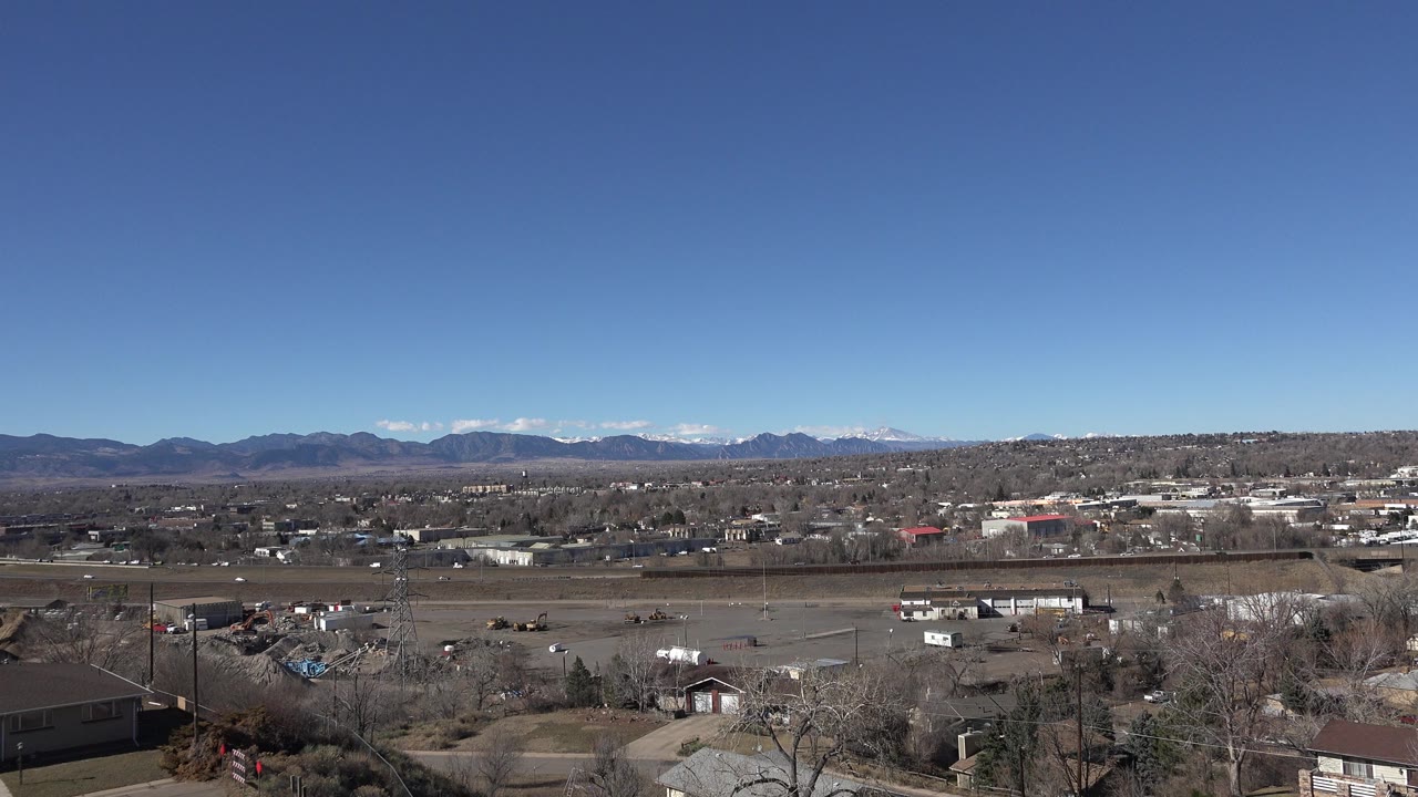 Wide 2015 Westminster, Colorado view with brown open ground, scattered buildings, leafless trees, distant mountains, and no visible people.