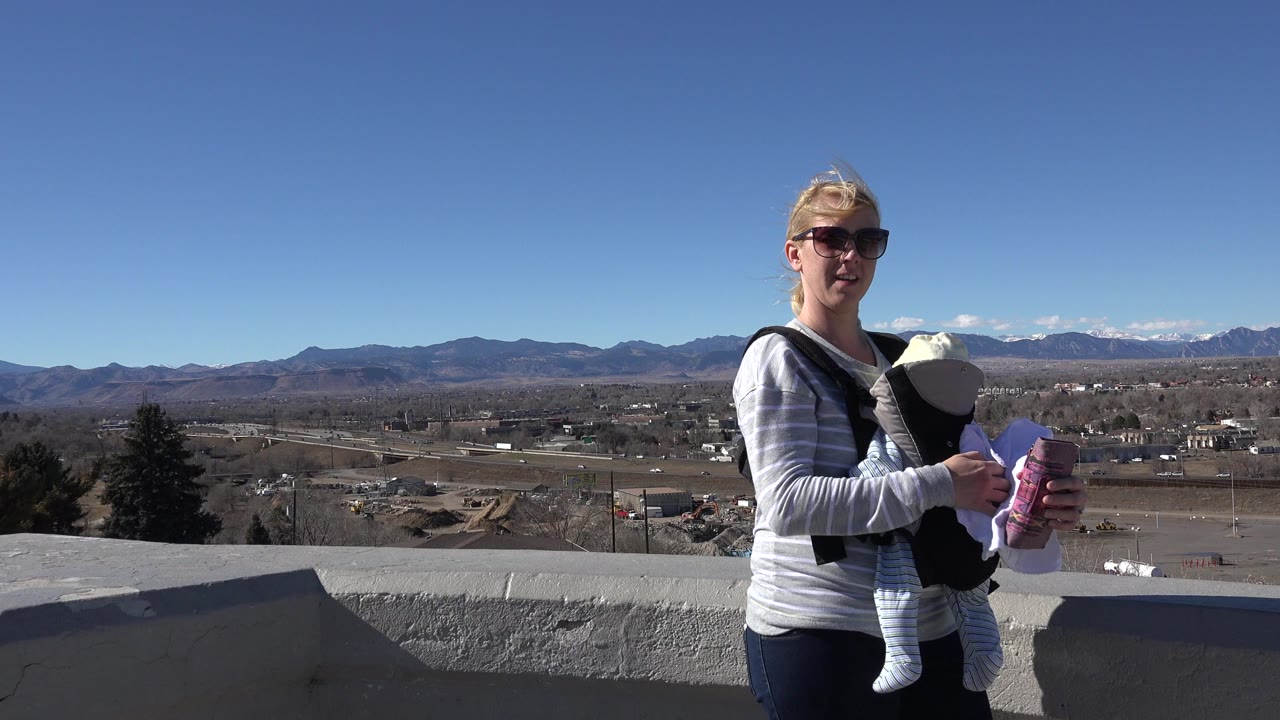 Blond woman in sunglasses holding a baby at an overlook.