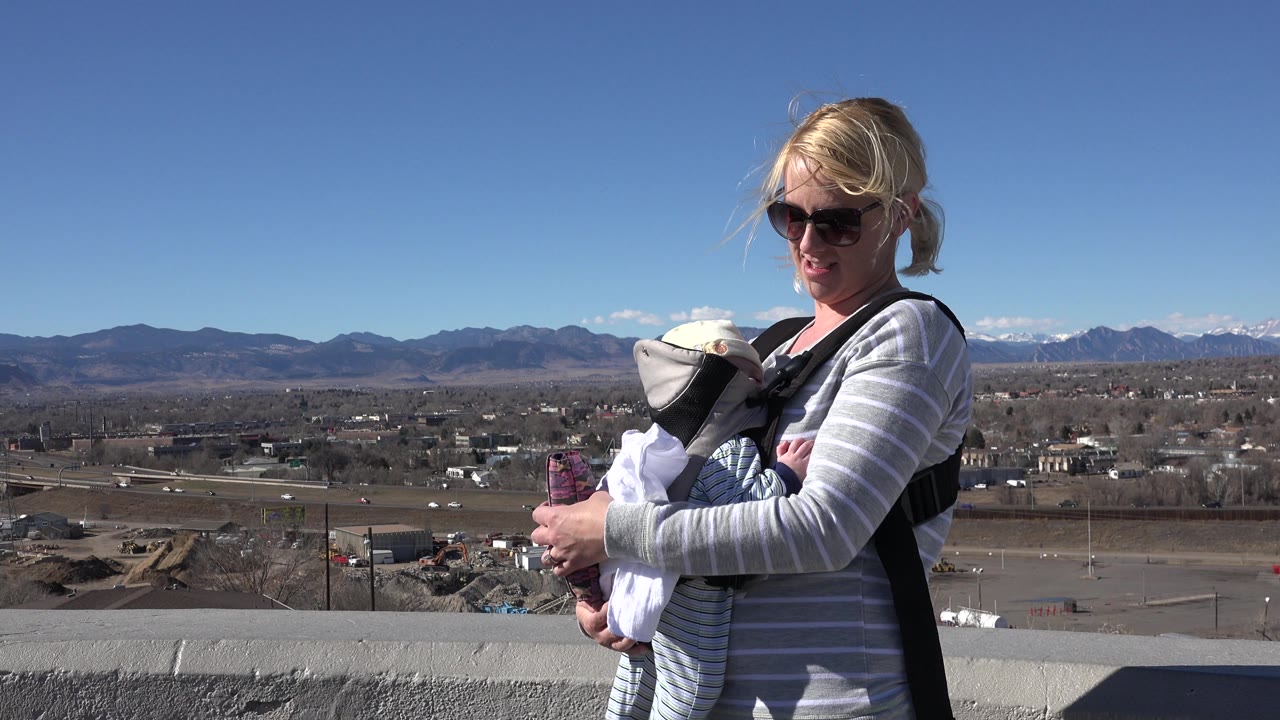 Woman with baby standing near a concrete wall above a suburban valley.