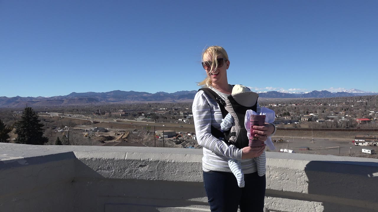Woman holding a newborn at an overlook with mountains behind her.