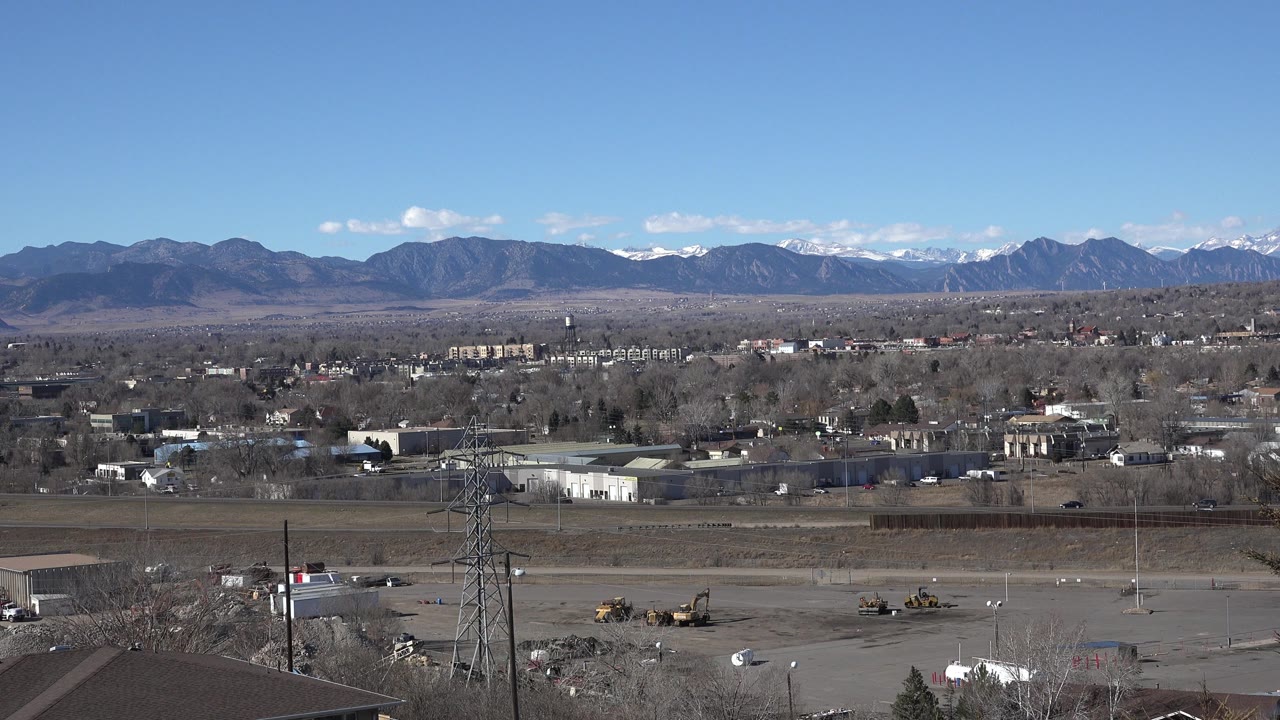 Wide suburban view with roads, buildings, utility towers, and distant mountains.