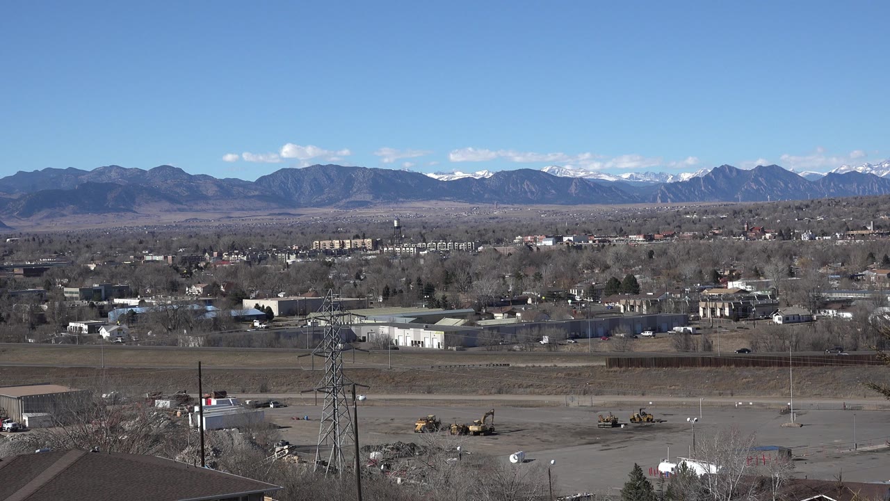 Second frame shows the Westminster panorama continuing across parking lots, low commercial buildings, scattered vehicles, and a broad mountain range, no visible people.