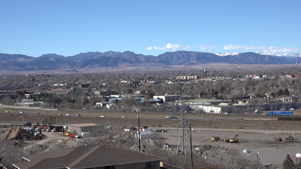 Roadside industrial area and utility tower below a distant mountain range.