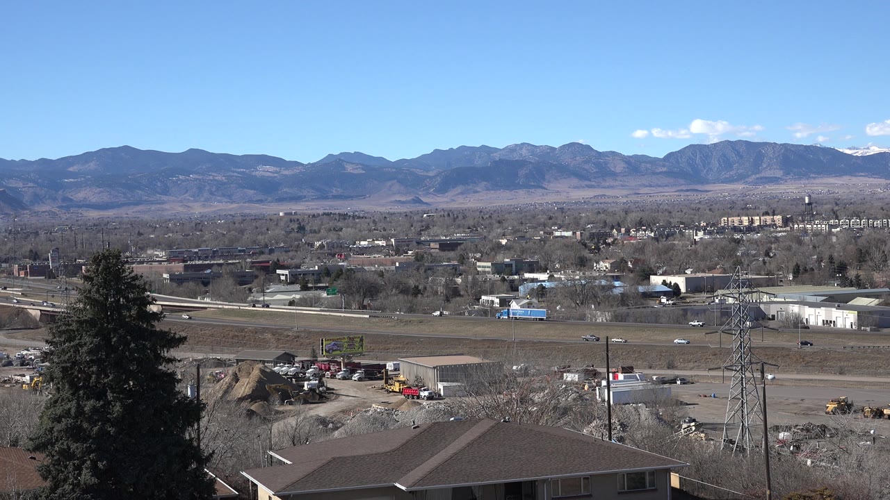 Clear blue sky over mountains, roads, industrial lots, rooftops, and a dark evergreen tree.