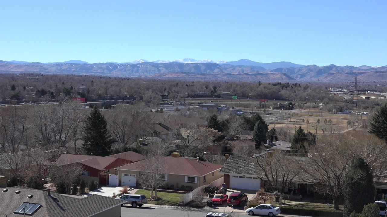Suburban rooftops and trees below distant mountains under a blue sky.