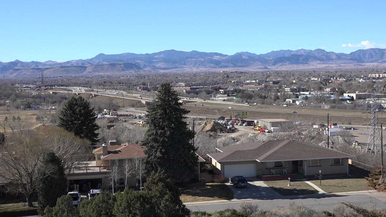 Opening frame of Westminster, Colorado with private homes in the foreground, a road and utility tower beyond them, and a blue mountain horizon in the distance.