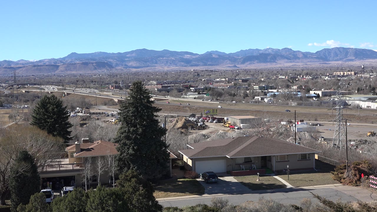 Homes and a large evergreen tree overlook roads, buildings, and mountains.