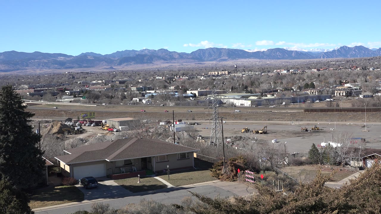Wide elevated view over houses, road, work yard, and distant mountains.
