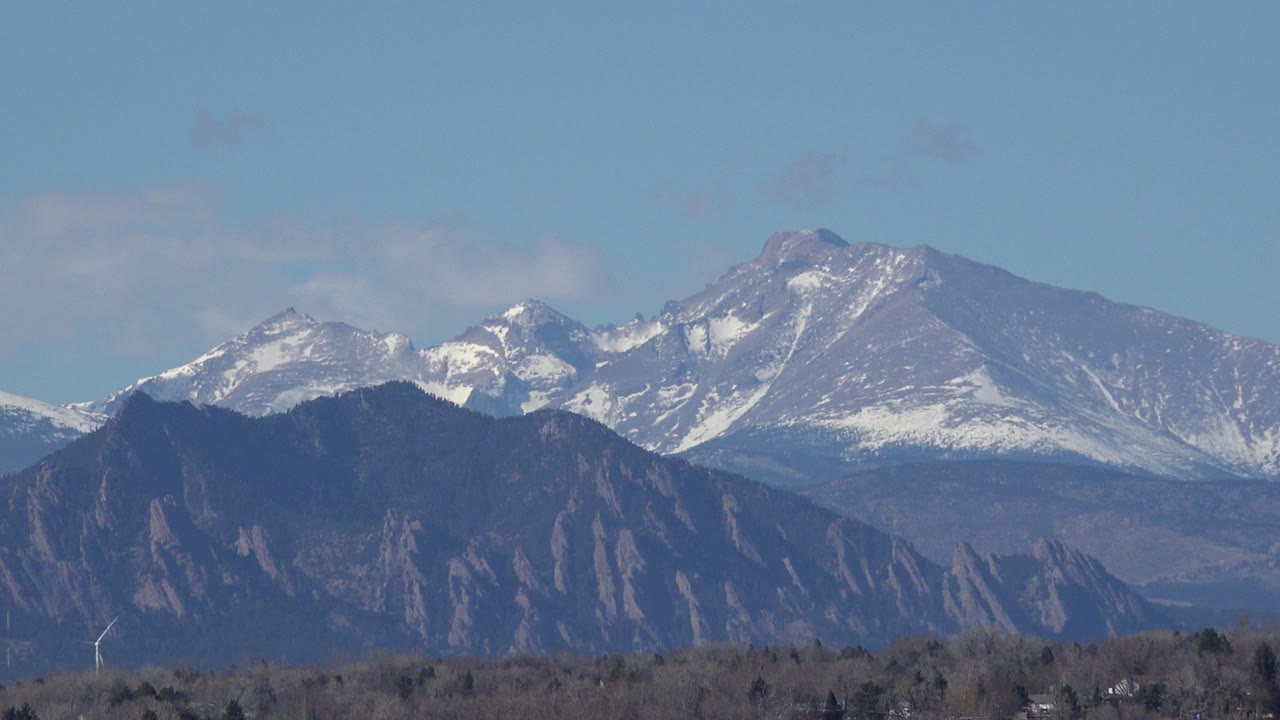 Opening frame of a Westminster, Colorado mountain view with snow on the rear peaks, a dark foothill ridge below, sparse trees near the bottom edge, and no visible people.