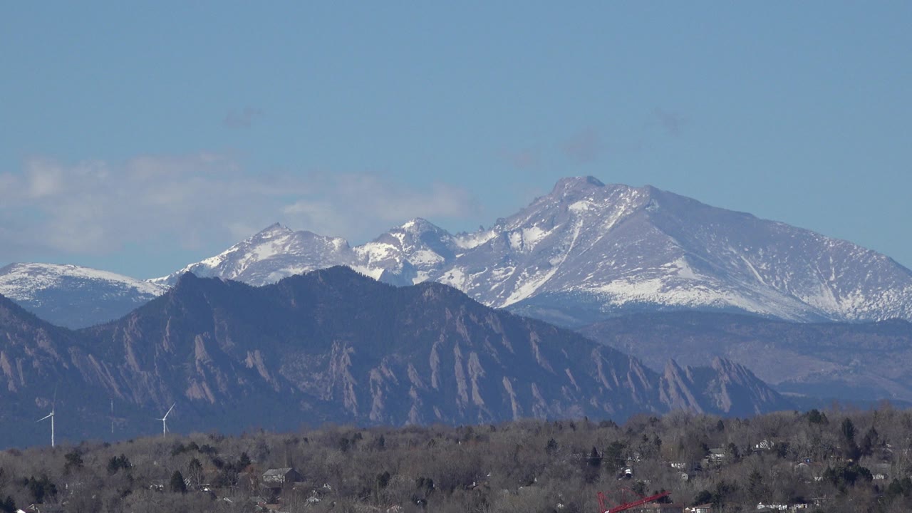 Snow-dusted mountains above dark foothills and a distant town under blue sky.