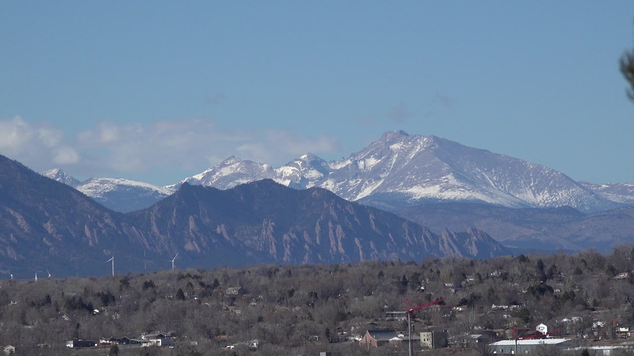 Wider Westminster, Colorado mountain view with several snow-dusted peaks, dark foothills, a distant suburban foreground, and no visible people.