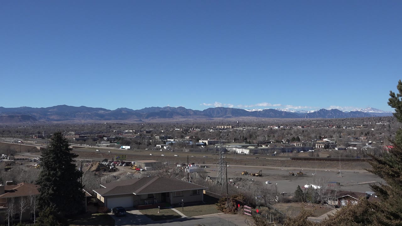 Suburban hillside view with a house roof in the foreground and mountains beyond a spread of roads and buildings.