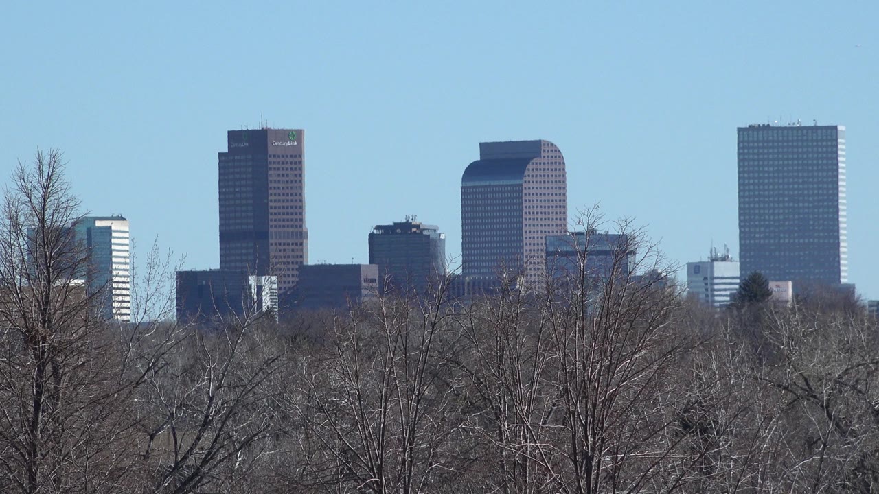 Brown and dark office towers remain centered behind leafless Westminster trees, with bright daylight and no visible people in frame.