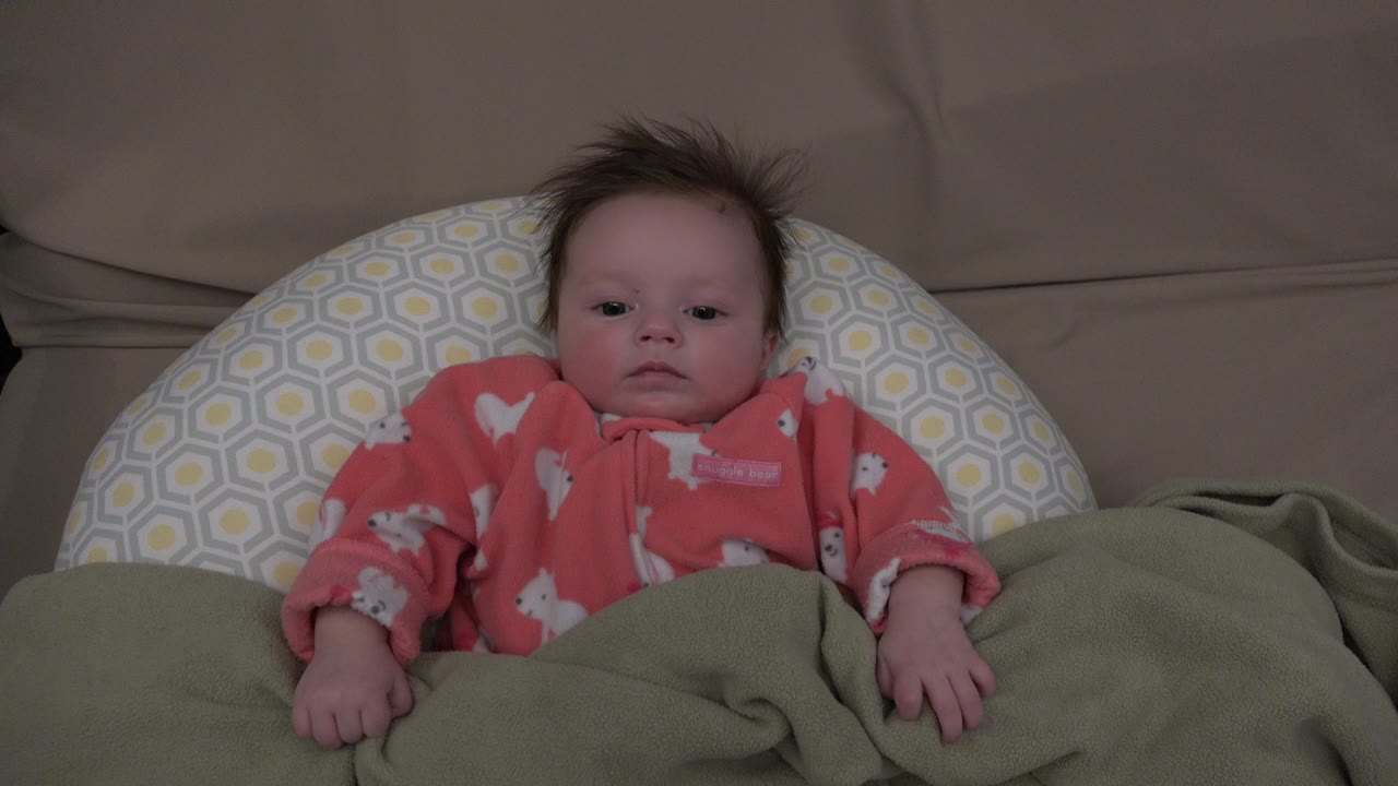 Infant in red pajamas lying on a pillow under a green blanket.