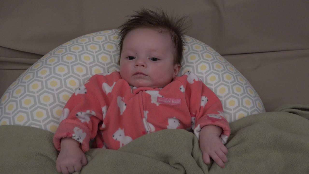 Baby leaning slightly against a patterned pillow on a couch.