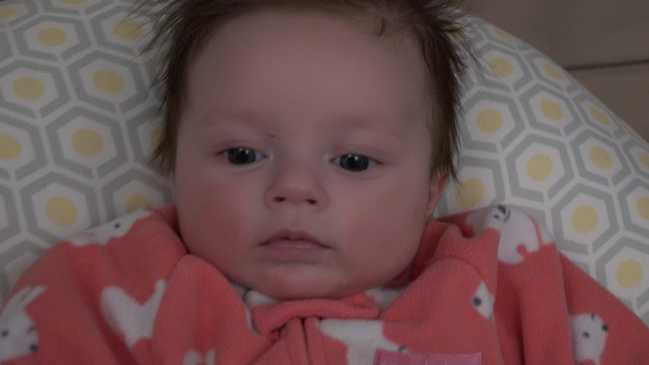 Baby lying on patterned bedding and looking toward the camera.