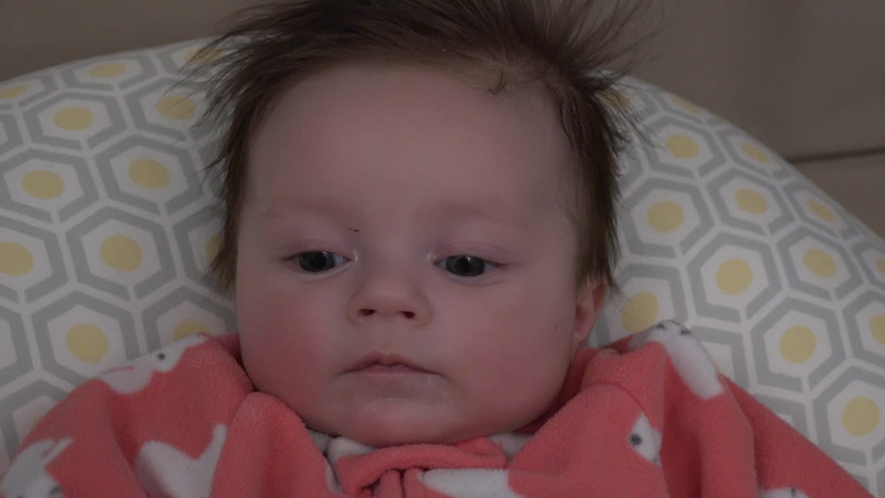 Baby glancing slightly downward while lying on the patterned cushion.