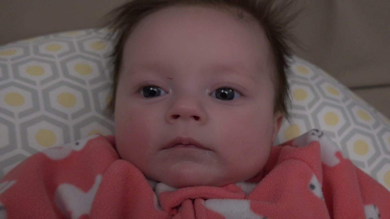 Baby lying on patterned pillow in coral fleece outfit.