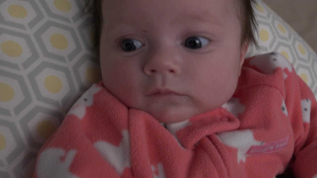 Baby looking to the side while lying on a patterned cushion.