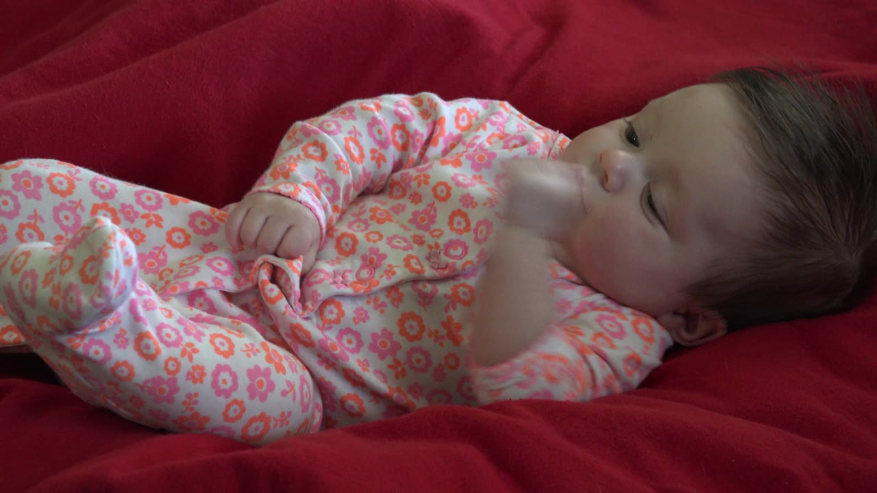 Baby on a red blanket with one blurred hand moving near the face.