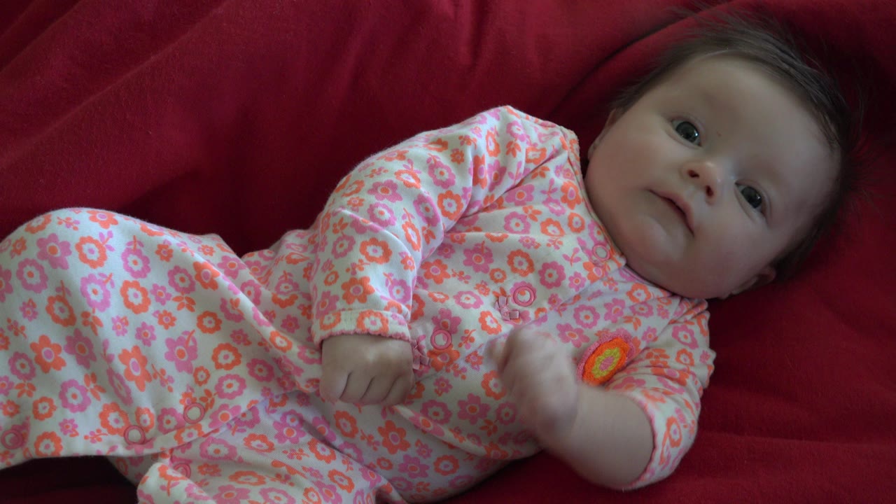 Baby in floral sleeper lying on a red blanket.