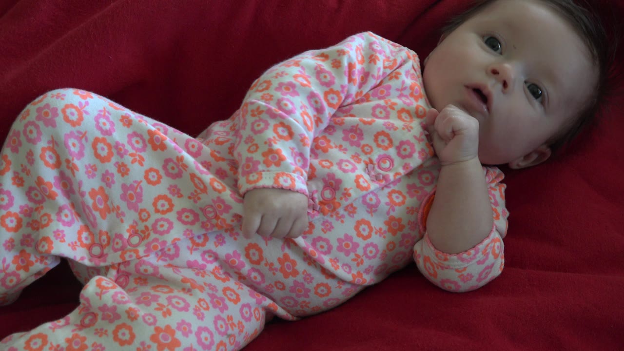 Baby on a red couch with legs lifted and face turned upward.