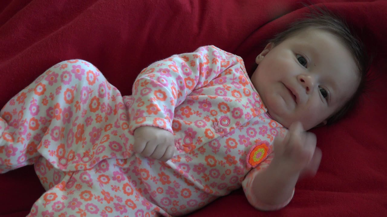 Baby in floral pajamas lying on a red blanket.