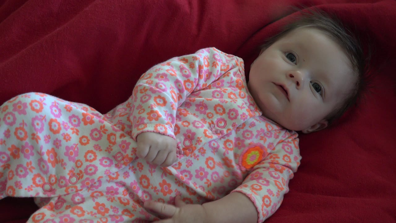Baby lying on red bedding in a floral sleeper.