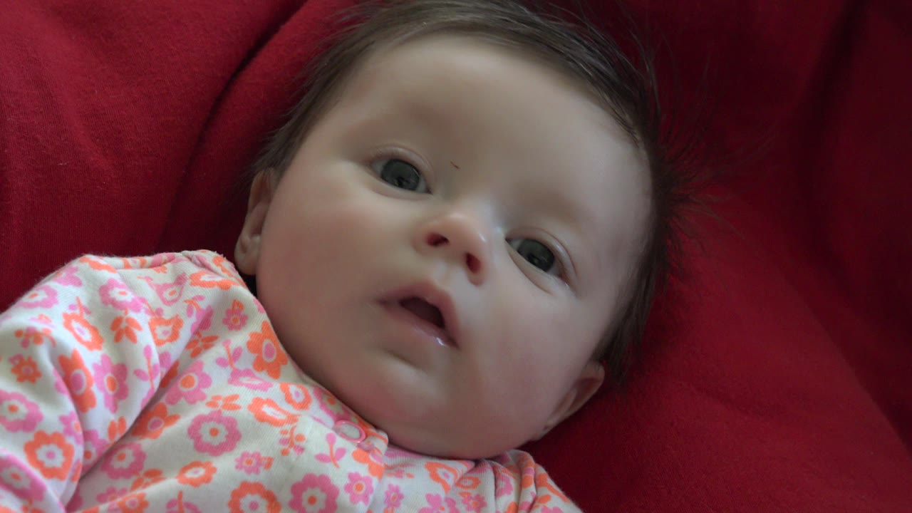 Baby lying on a red blanket in a floral shirt.