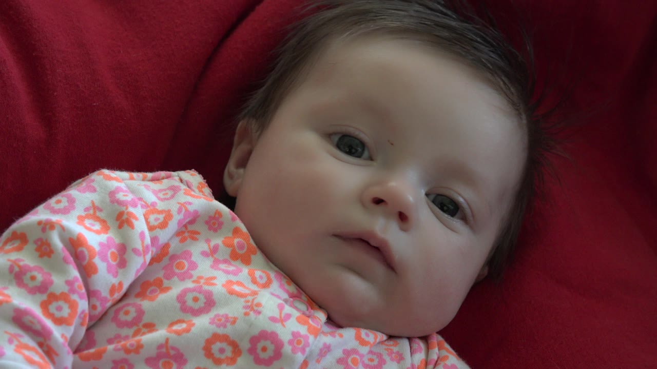 Baby in pink floral onesie lying on red fabric.